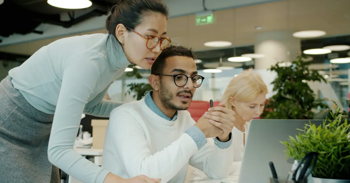 Two colleagues discussing information on a computer screen in a shared office.