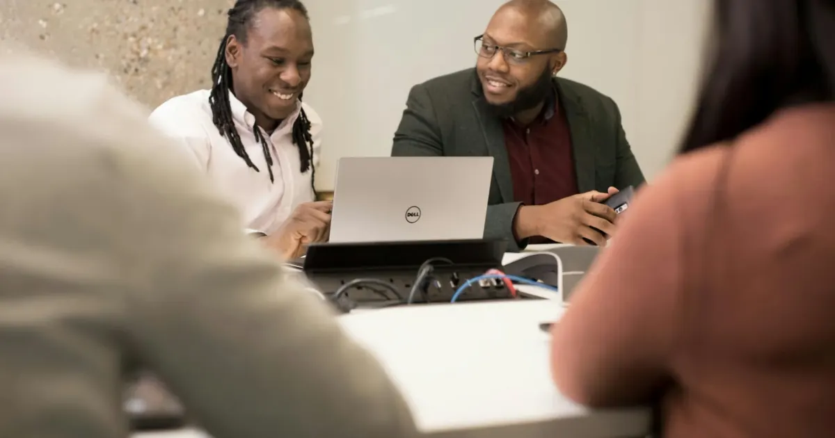 A group discussing shared work around a laptop at a meeting table.