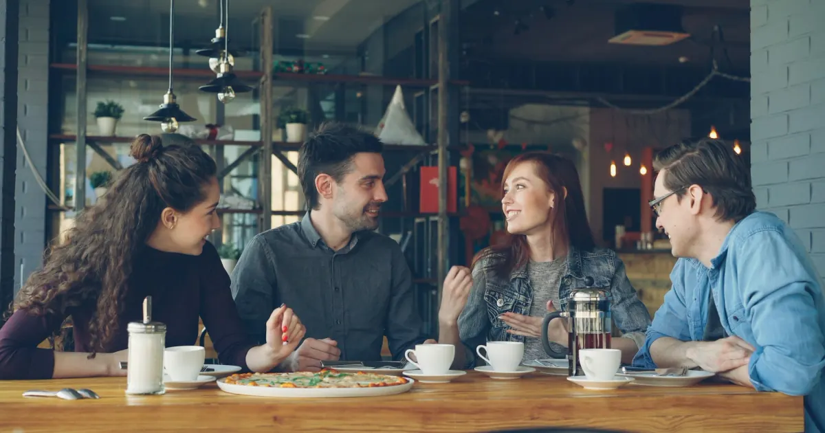 Friends talking together over drinks at a cafe table.