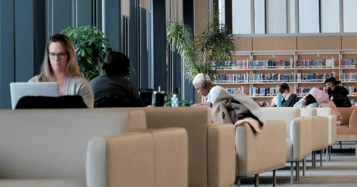 People studying at desks in a modern university library with large windows.