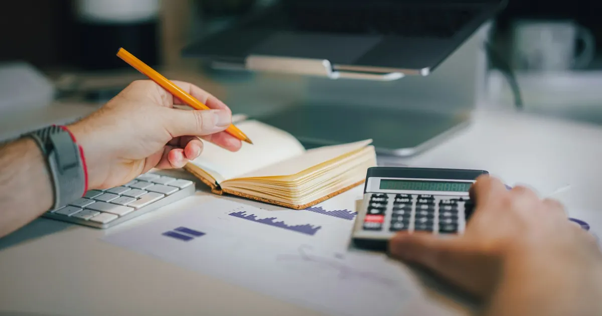 A person reviewing figures with a calculator and notebook at a desk.